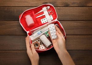 Woman taking pills from first aid kit at wooden table, top view